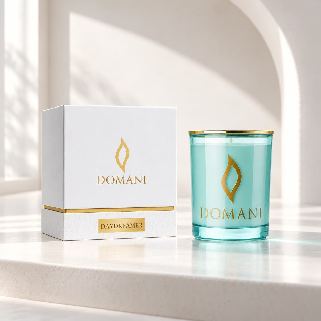 Domani daydreamer candle in Aquamarine glass, beside its named box in a sunlit ivory alcove. Also available in the other three jar colors.