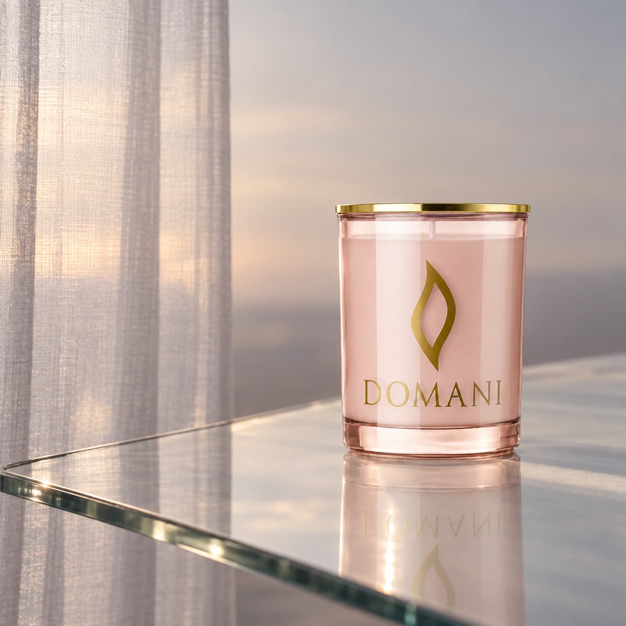 Domani forever and a day candle in Rose Quartz glass, on a diagonal glass tabletop beside a sheer curtain. Also available in the other three jar colors.
