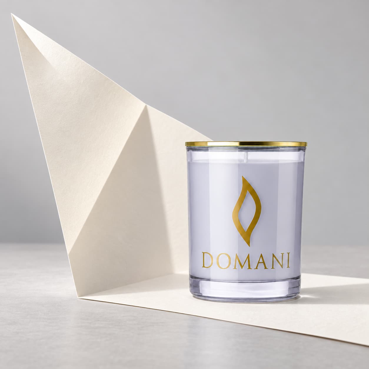 Domani love letter candle in Sapphire glass, beside a folded ivory paper sheet. Also available in the other three jar colors.