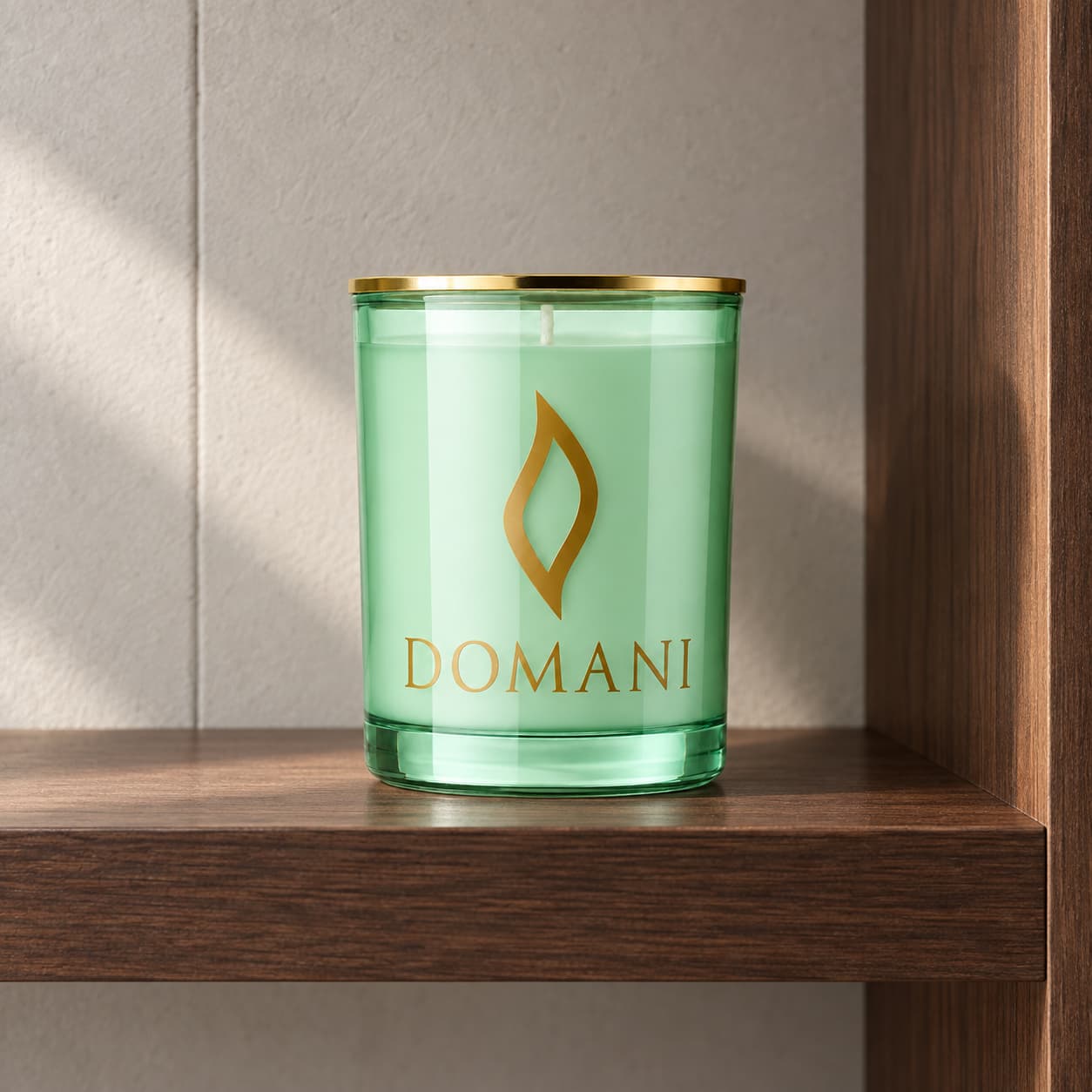 Domani novella candle in Emerald glass, on a walnut shelf against pale plaster. Also available in the other three jar colors.