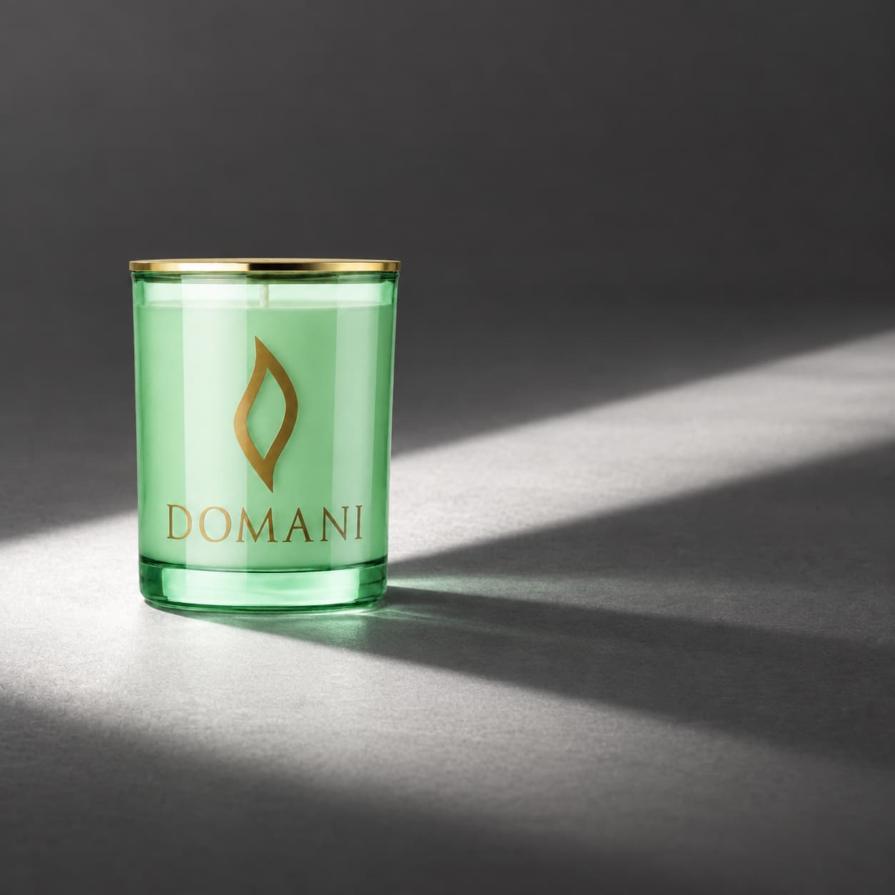 Domani philos candle in Emerald glass, on an open charcoal floor crossed by a neutral light band. Also available in the other three jar colors.