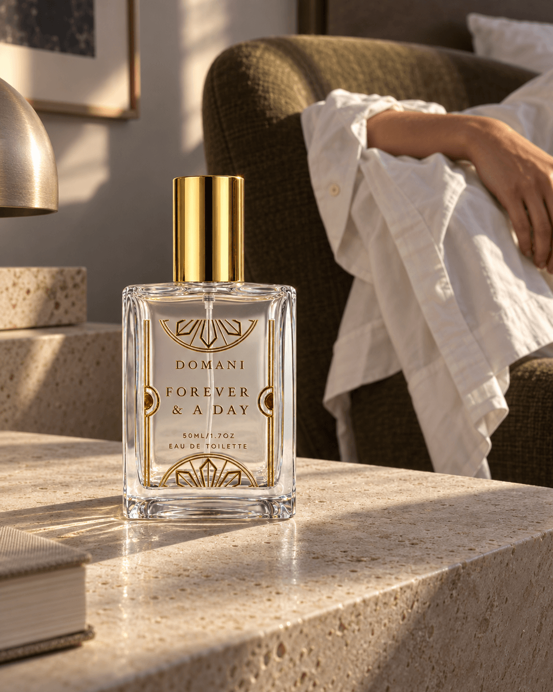 The capped Forever & A Day 50 ml perfume on a pale stone bedside table, with olive upholstery and a resting forearm in a loose white shirt behind it.
