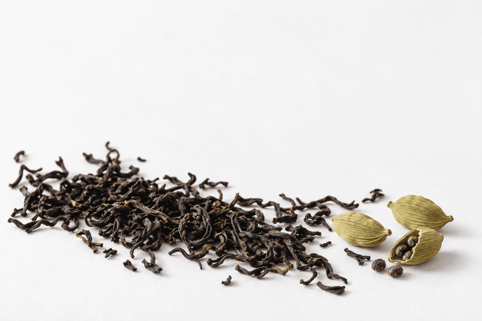 Dark curled tea leaves meeting pale ribbed cardamom pods, one split open beside loose seeds.