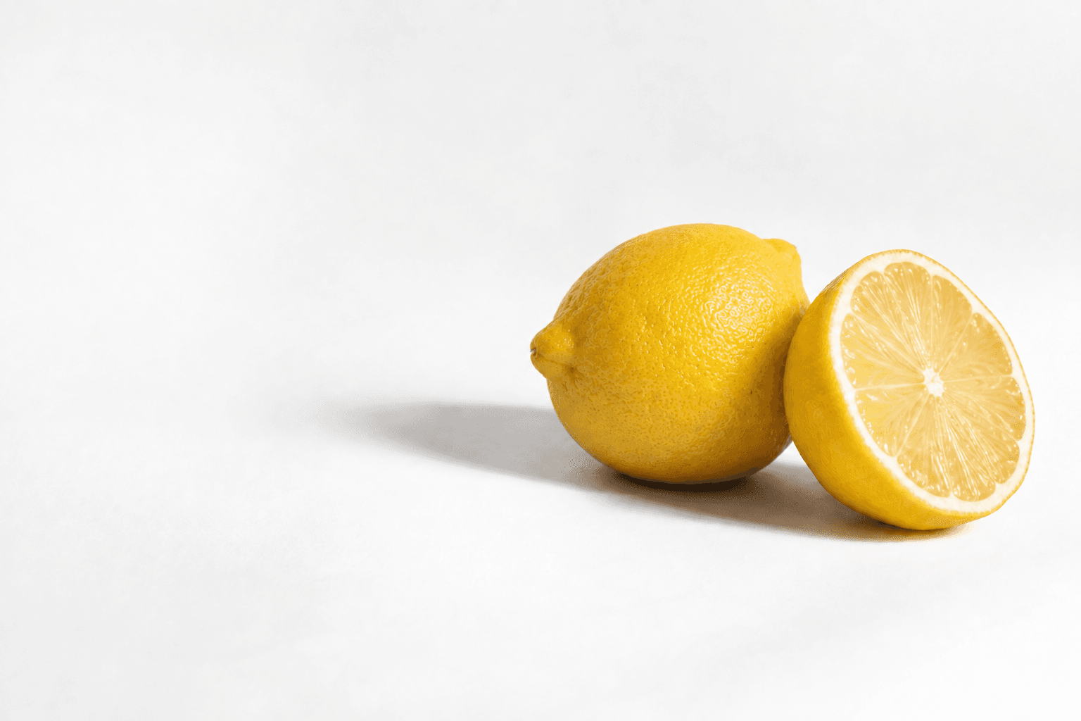 A whole yellow lemon and a cut lemon half resting on white paper.