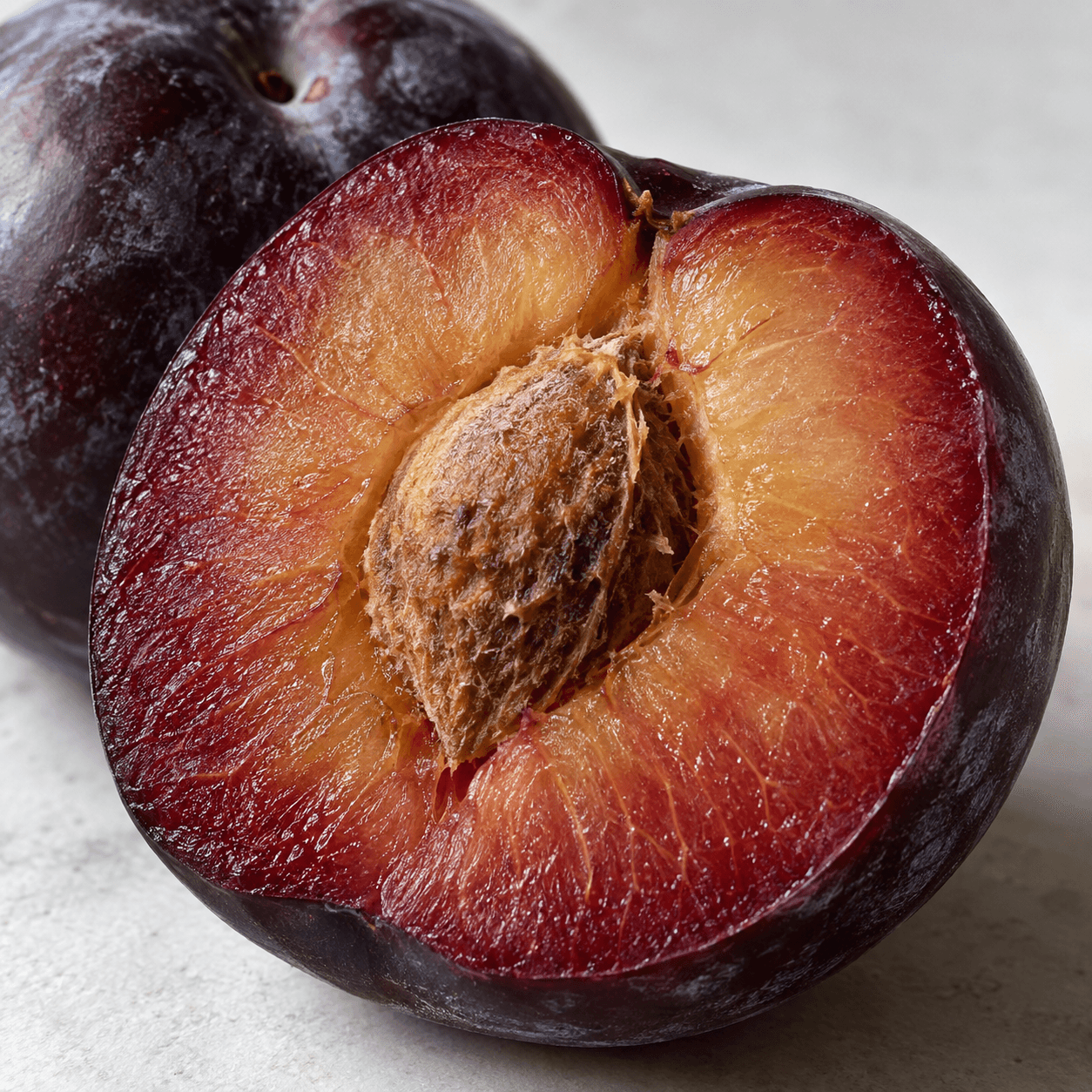 A close view of a cut dark-purple plum with red-gold flesh, fibrous stone and waxy skin.