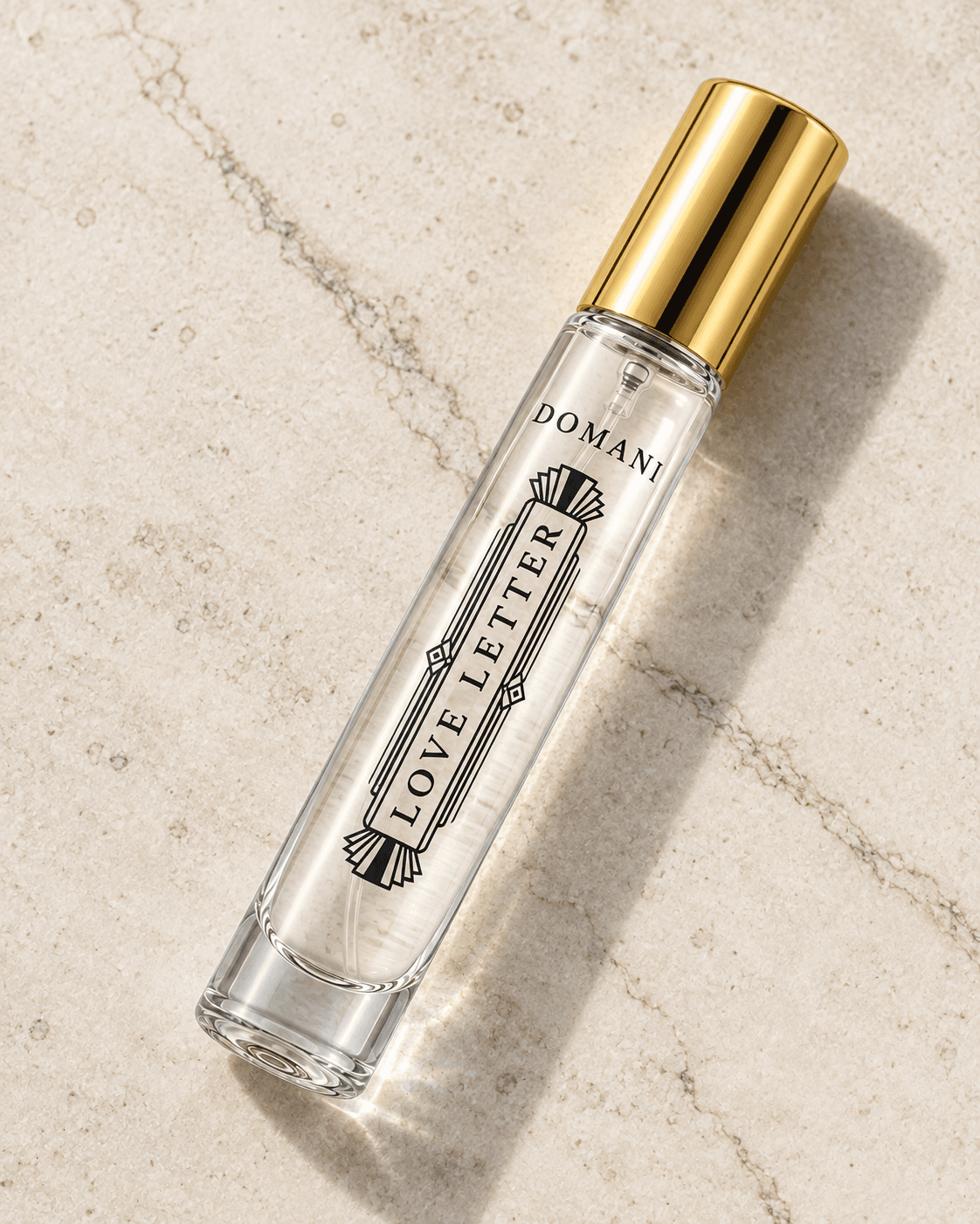 Love Letter 10 ml clear travel vial reclining diagonally on pale limestone, showing black artwork and a gold cap.