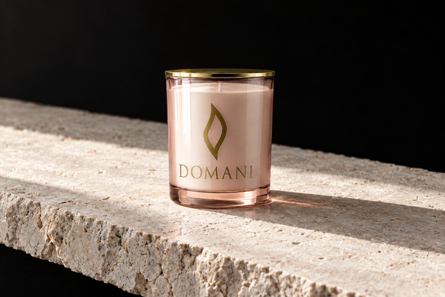 A Domani candle in translucent Rose Quartz glass with white wax and its gold lid rests on pale limestone against black, with a directional contact shadow.